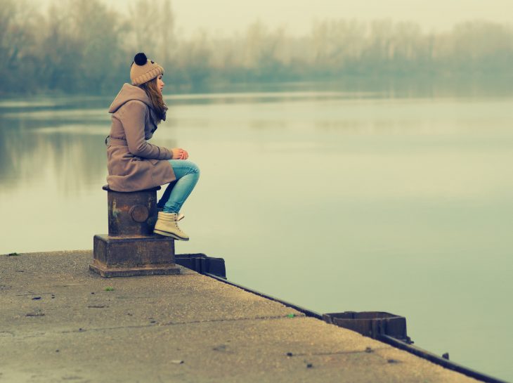 Chica reflexionando a la orilla de un lago 