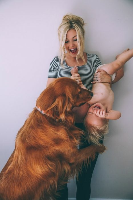 Chica sosteniendo a un bebé de cabeza y jugando con un perro 