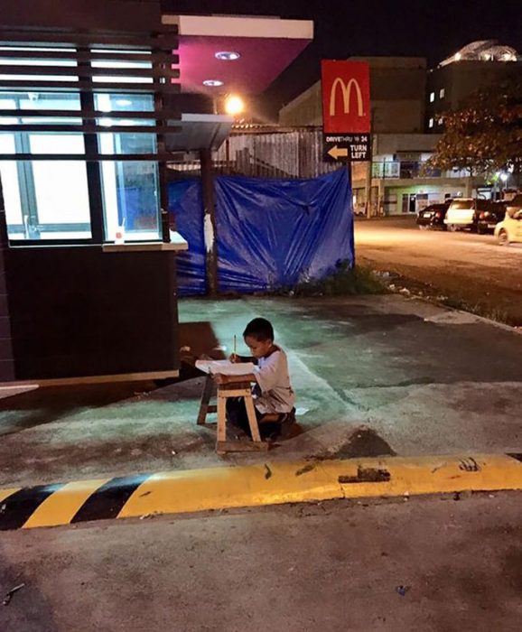 Niño sin hogar hace su tarea con la luz de un local 