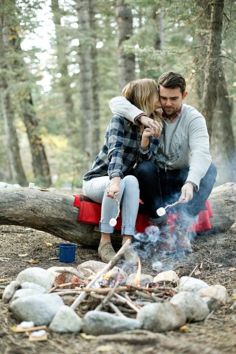 Pareja de novios asando malvaviscos en un campamento 