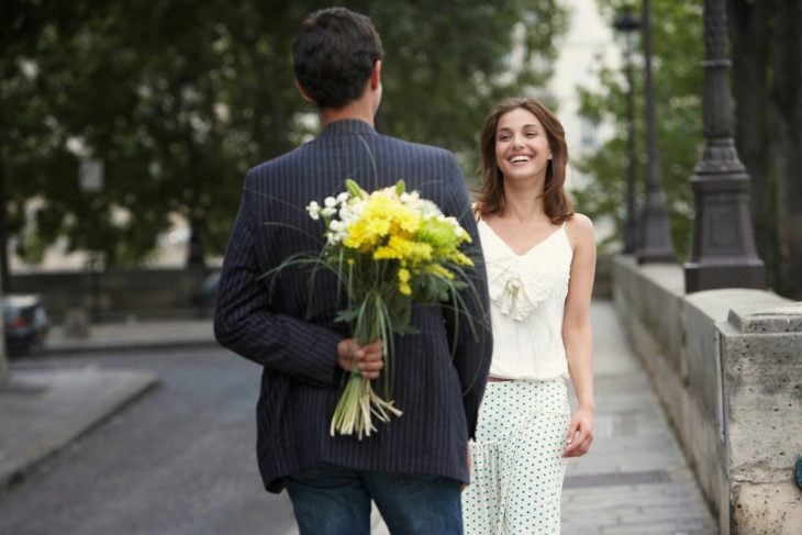 Hombre oculta ramo de flores a chica que sonríe