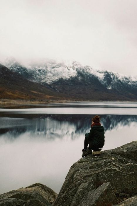 Chica sentada en una montaña viendo un lago 