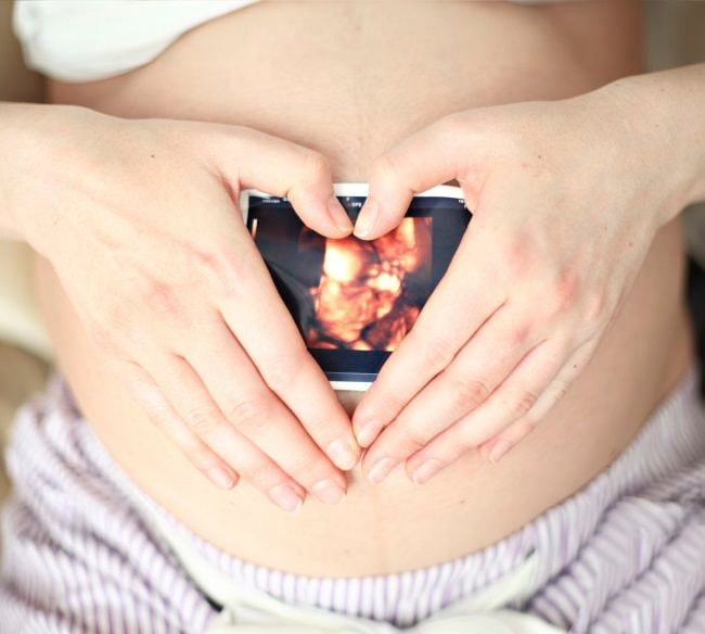 Sesión de fotos de maternidad mamá sosteniendo una ecografia de su bebé sobre su vientre 