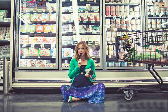 Sesión de fotos de maternidad chica sentada en un supermercado comiendo nieve 