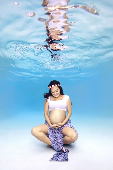 Sesión de fotos de maternidad bajo el agua chica tocándose el vientre 
