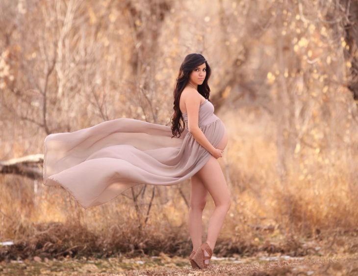 sesiòn de fotos de maternidad chica en un bosque con un vestido mostrando su vientre 