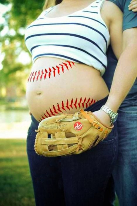 Sesión de fotos de maternidad chica con su vientre pintado como una pelota de beisbol 