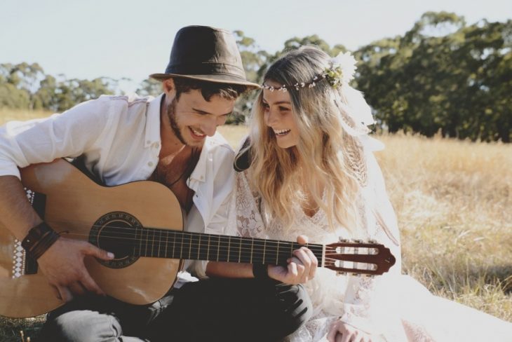 Chico sentado junto a una chica tocando la guitarra y riendo 