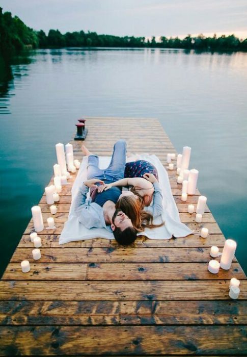 Pareja de novios recostados sobre una alfombra en un muelle rodeados de velas 