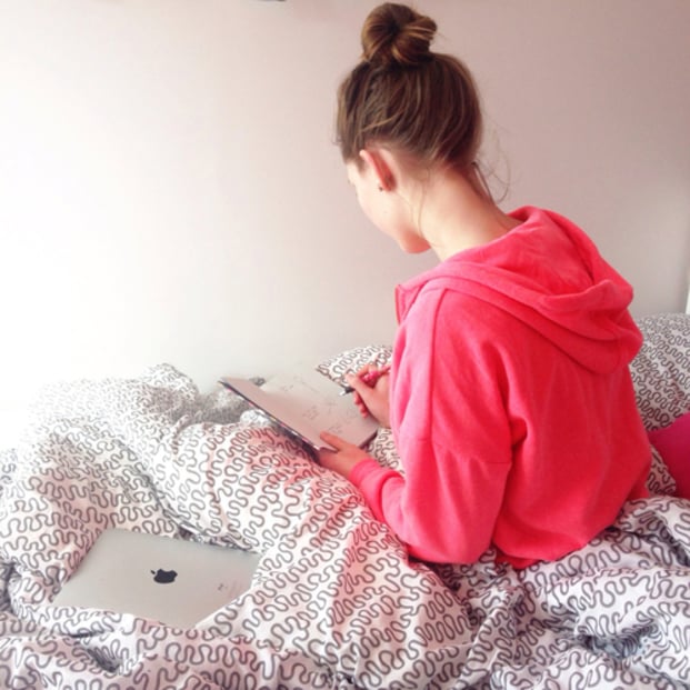 Chica anotando cosas en una agenda mientras esta sentada en su cama 
