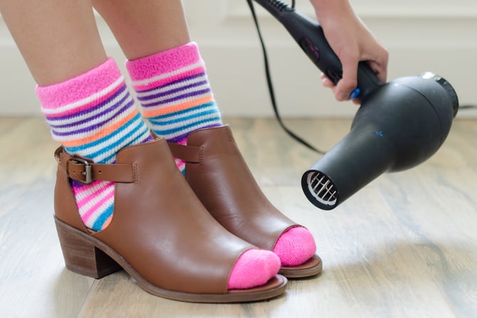 mujer calentando zapatos con secadora de cabello
