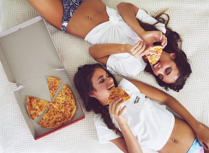 Chicas recostadas en la cama comiendo pizza 