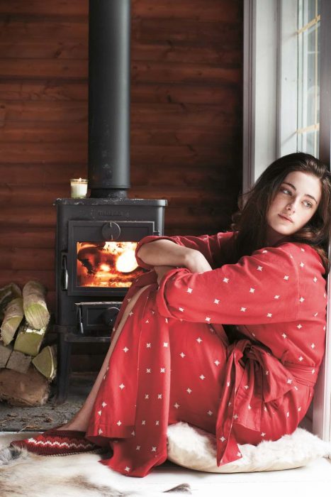 Chica sentada frente a una chimenea viendo hacia la ventana y pensando 