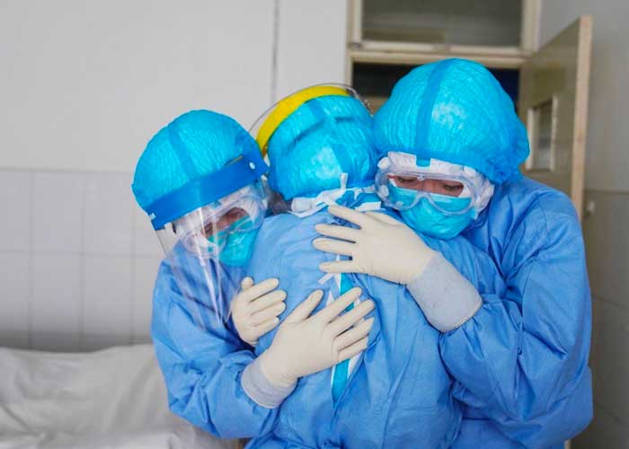Grupo de enfermeras con trajes de protecciòn contra Covid-19, abrazadas dentro de una sala de hospital 