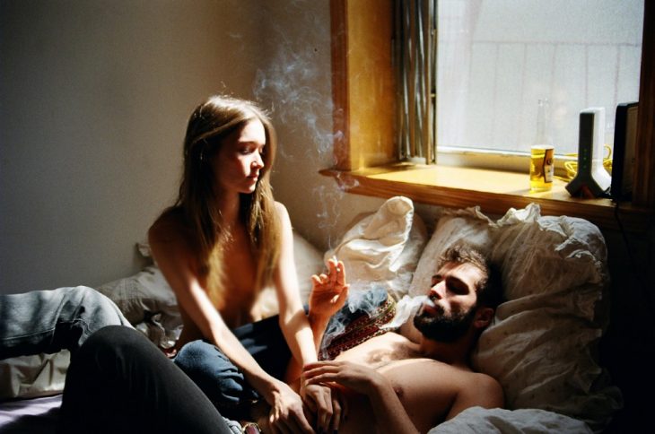 Pareja de novios fumando un cigarrillo mientras están en la cama 
