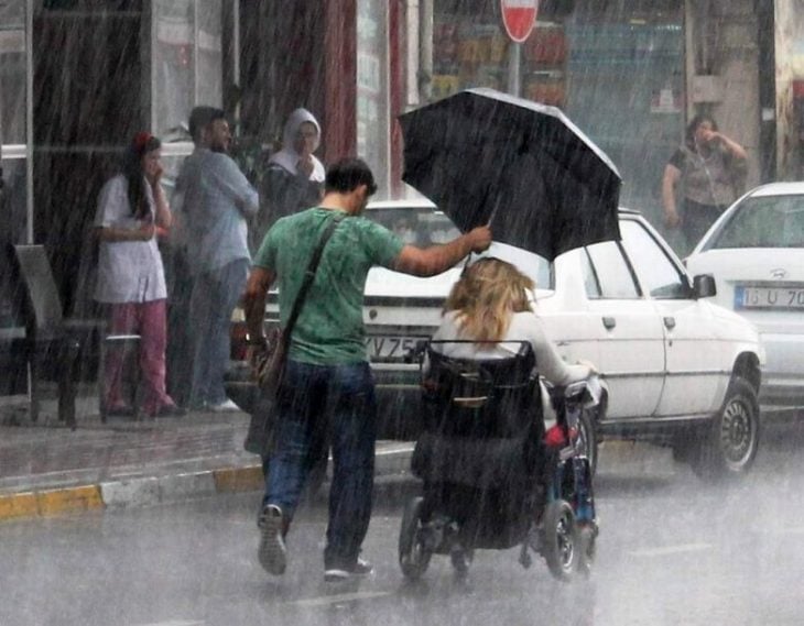 chico cubriendo con paraguas a mujer en silla de ruedas