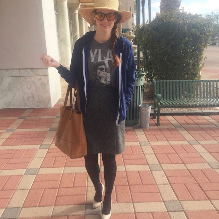 Chica usando una falda y camisa gris un sombrero, lentes y zapatos de tacón 