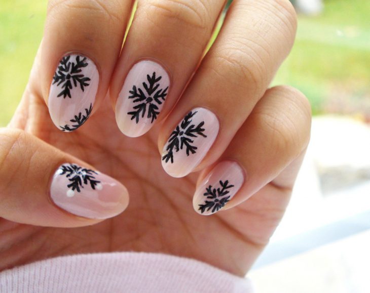 Diseño de uñas navideñas pintadas en color rosa con copos de nieve color negro 