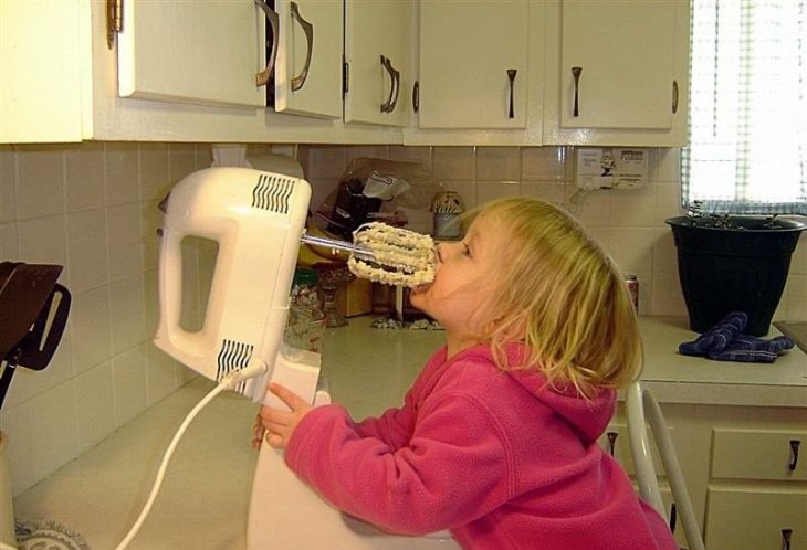 Niña lamiendo las aspas de una batidora con mantequilla 