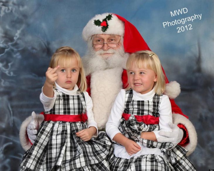 Niña haciendo señas obsenas mientras esta en una foto con santa claus 