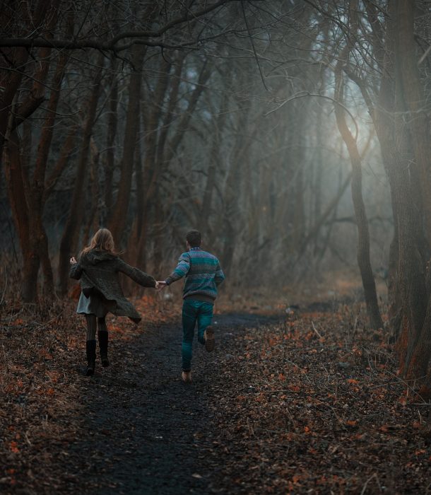 Pareja de novios corriendo tomados de las manos entre un bosque 