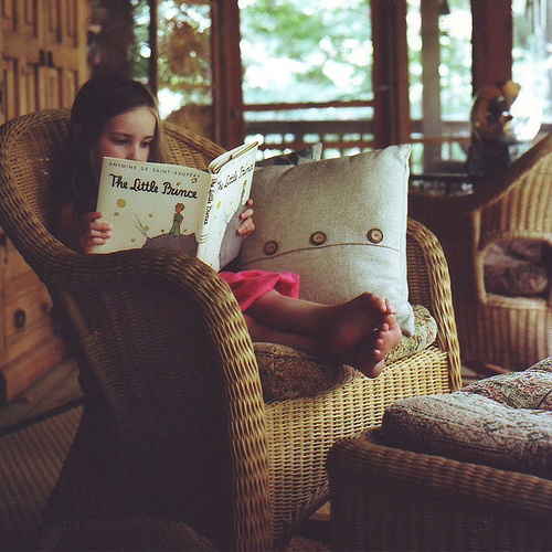 Niña leyendo un libro sentada en un sofá