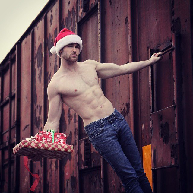 Chico usando un gorro de santa claus parado sobre un tren y sosteniendo regalos 