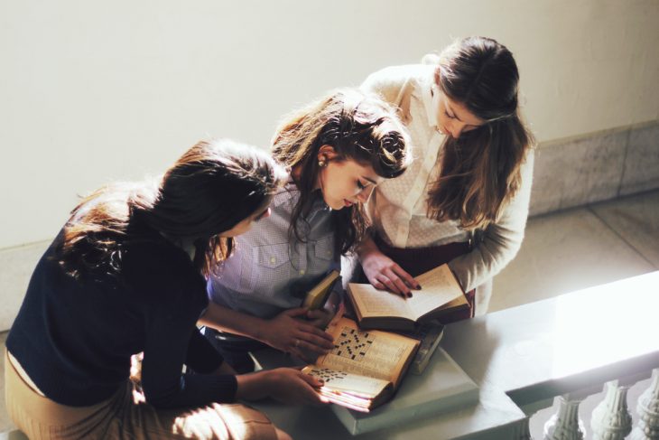 Chica junto a otras dos mientras están viendo un libro 