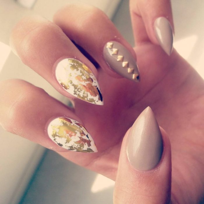 Uñas con un diseño de pico de montaña en color nude con flores café y doradas 