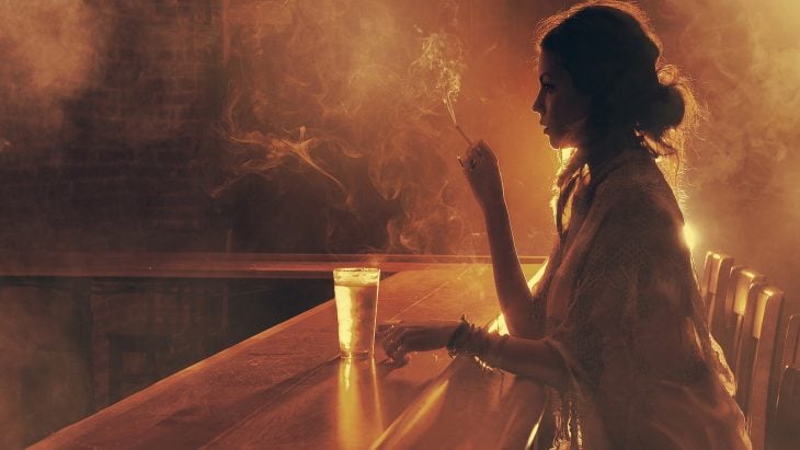 Chica fumando un cigarrillo en la barra de un bar 