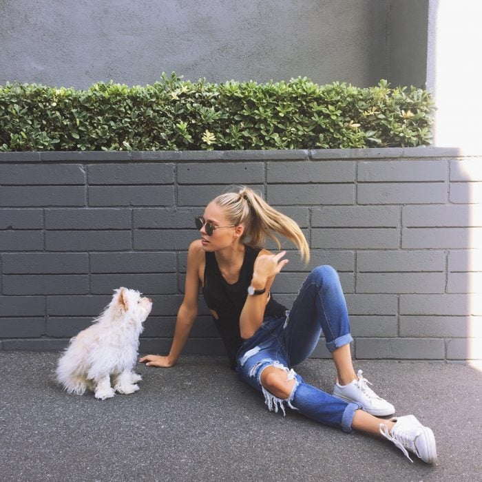 Chica sentada junto a un perro mientras están sentados en la acera de la calle