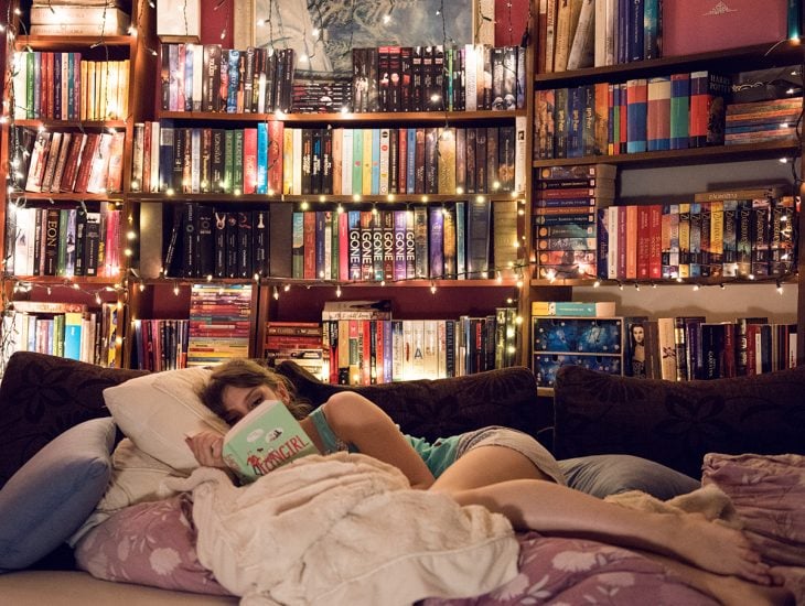 Chica recostada en la cama leyendo un libro 