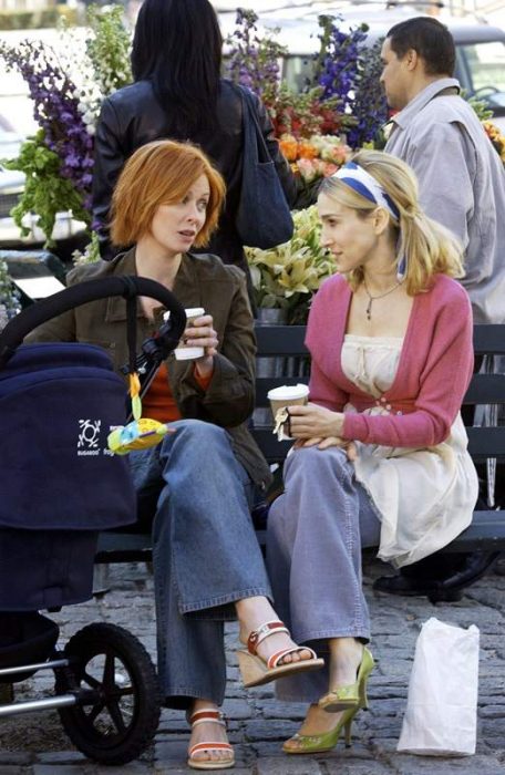 Escena de la serie sex and the city. Miranda y carrie sentadas en un parque conversando 