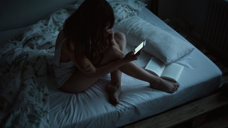 Chica sentada en la cama con el celular en la mano 
