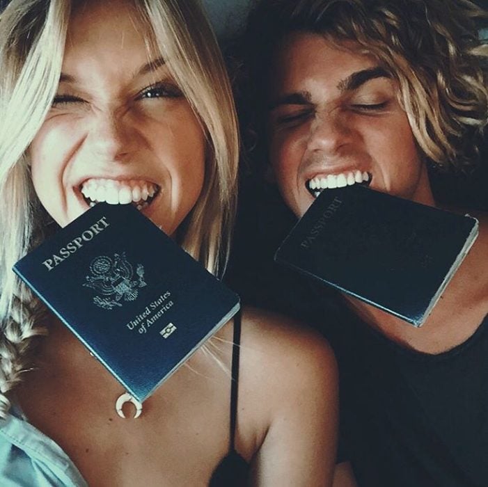 Pareja de novios sosteniendo un pasaporte en su boca 