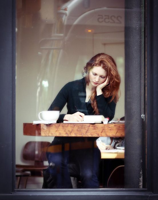 Chica sentada en un café mientras escribe un libro 