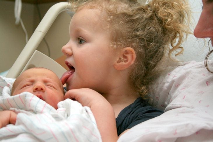 niña pasa la lengua por cara de su hermano recién nacido