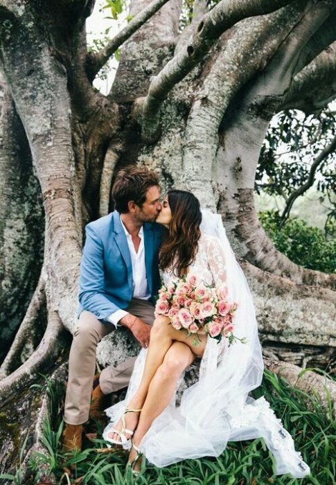 Pareja recién casada besándose en un árbol 