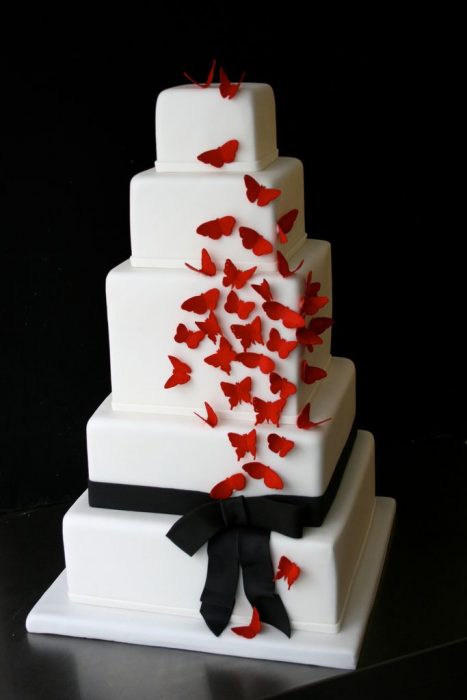 Pastel de boda de color blanco con un moño negro y mariposas de color rojo 