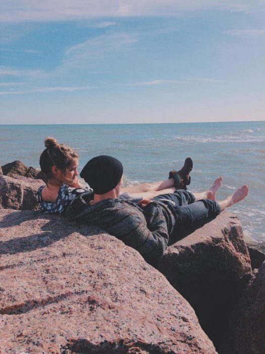 Pareja platicando en unas rocas frente a la playa 