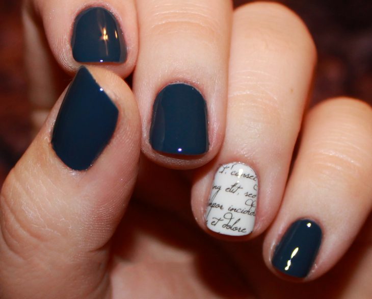 Uñas con diseños minimalistas en color azul con una uña en blanco con letras en negro 