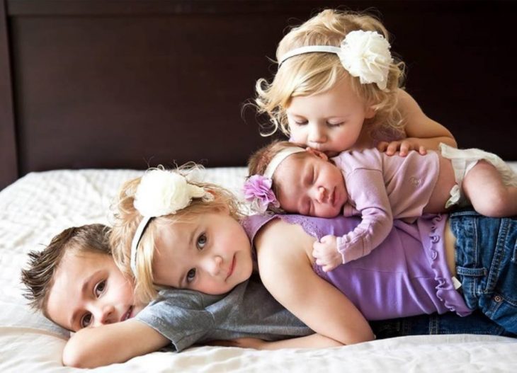 Hermanos dormidos uno sobre el otro mientras están en una cama posando para una fotografía 