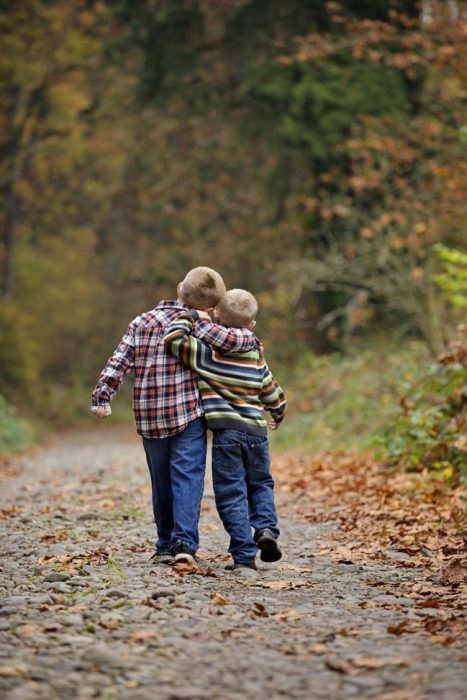 Hermanos abrazados mientras caminan por en medio de un bosque 