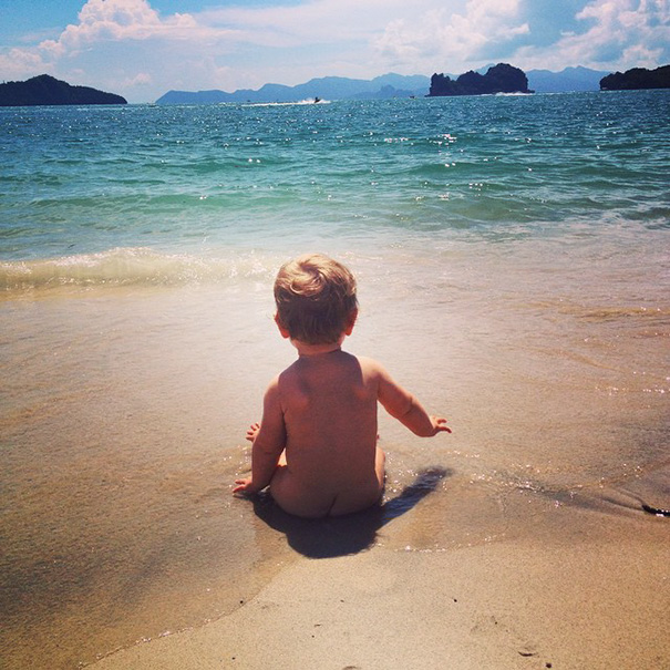 Bebé que ha viajado por el mundo sentada en la arena de la playa viendo el mar 