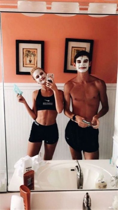 Pareja de novios poniéndose mascarillas en la cara y tomándose fotos en el baño 