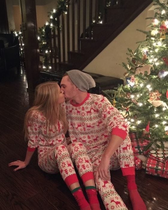 Pareja de novios frente al árbol de navidad usando la misma pijama mientras abren regalos 