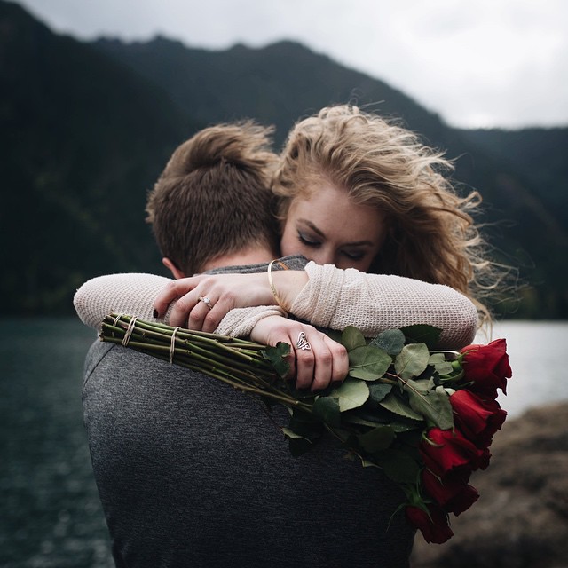 Chico abrazando a una chica mientras le regala un ramo de rosas