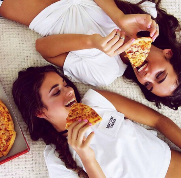 Chicas recostadas en el suelo comiendo pizza 