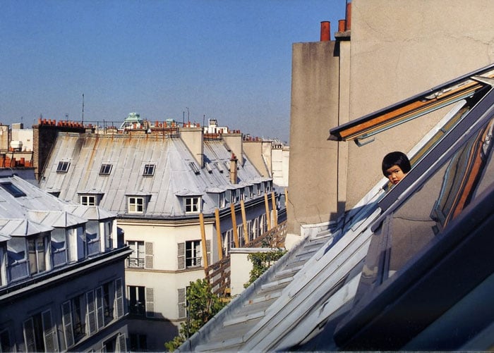 Kotori Kawashima fotografiando a una niña mientras se asoma por la ventana de un edificio 