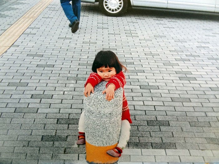 Kotori Kawashima fotografiando a una niña mientras ella se sujeta de un poste 
